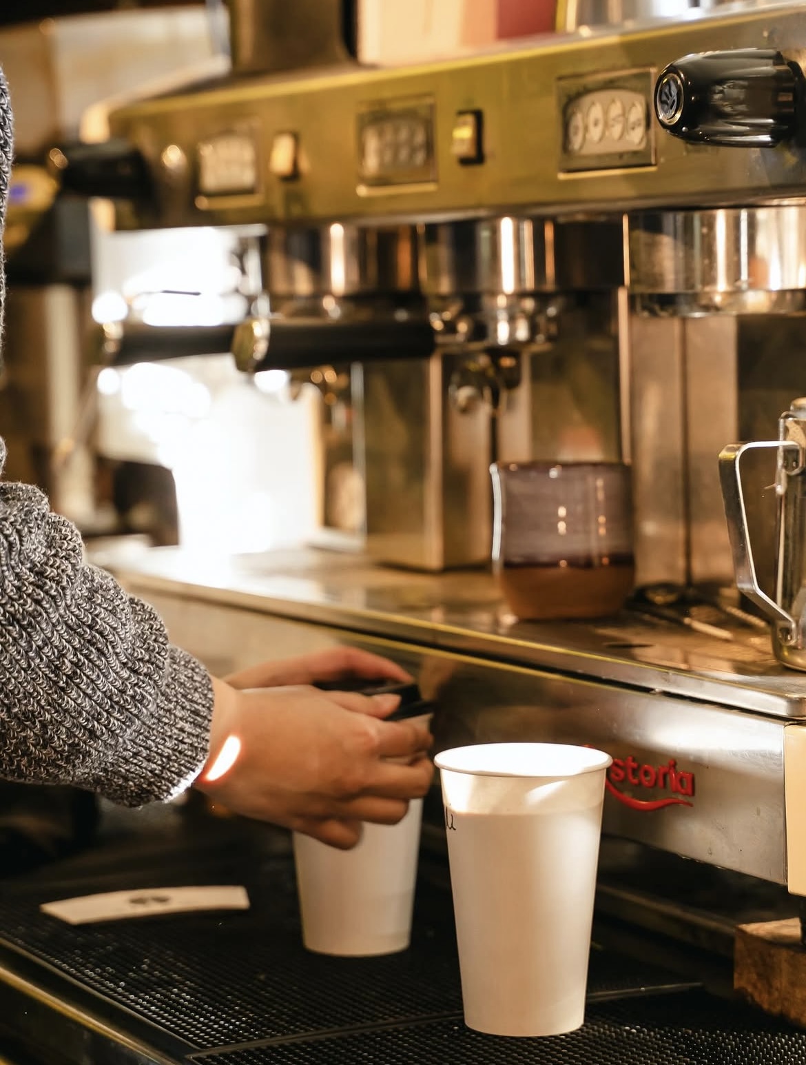 A barista pulling espresso shots into paper cups behind the machine