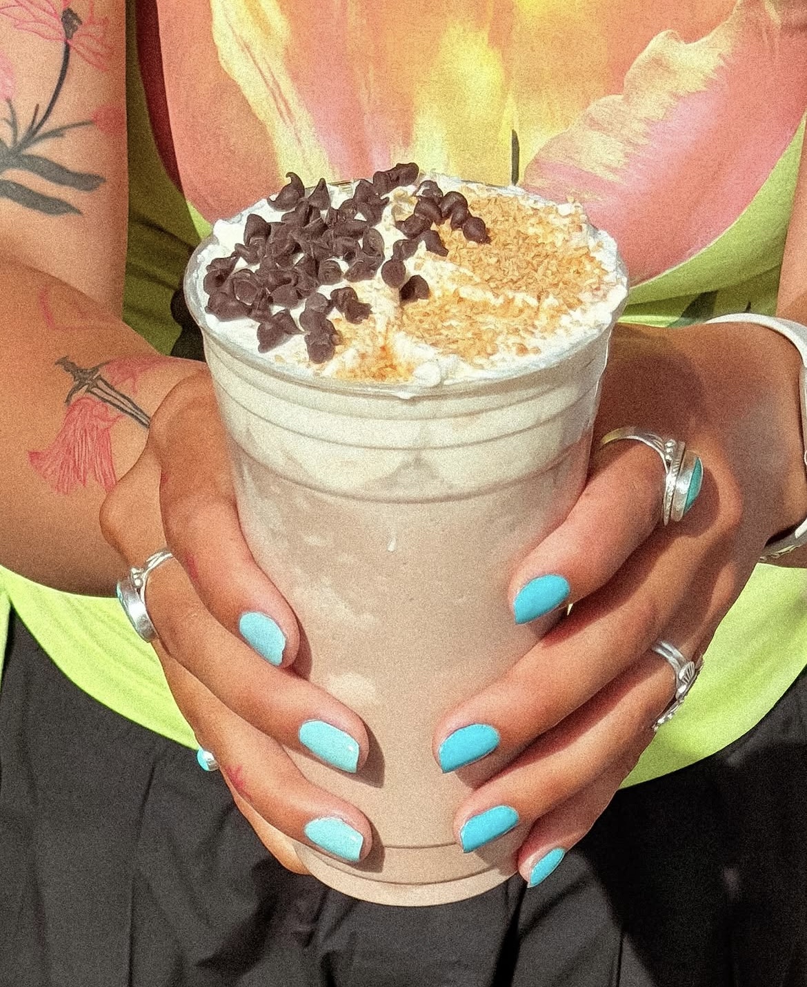 Hands cradling a whipped cream topped drink with toasted coconut and chocolate chips