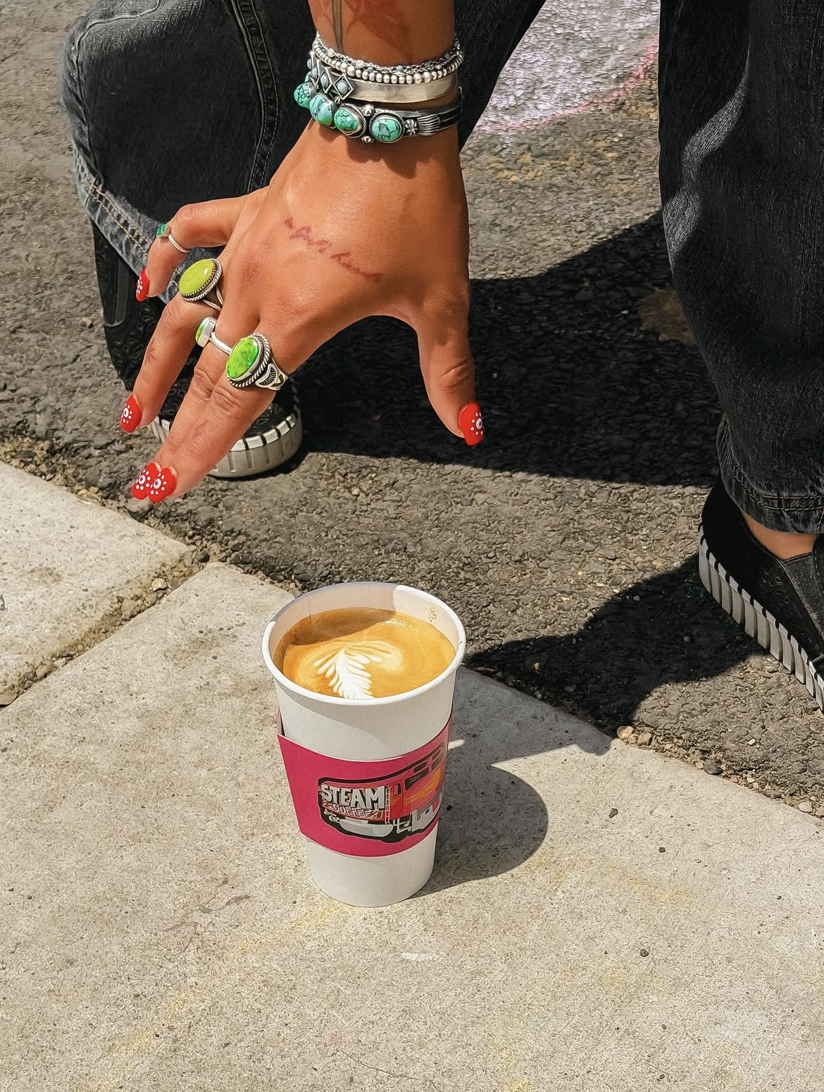 A latte with feathered art set down on the sidewalk outside Steam