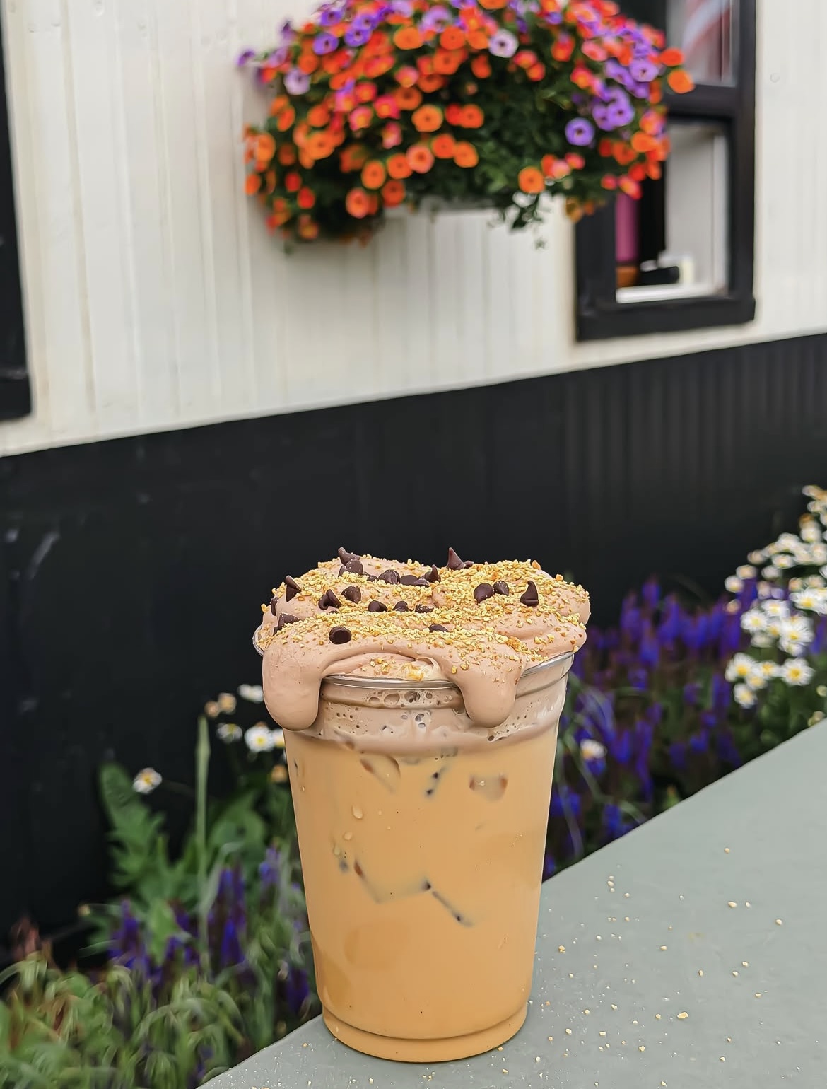 Iced signature drink piled with whipped cream, chocolate chips, and gold sugar, on the patio